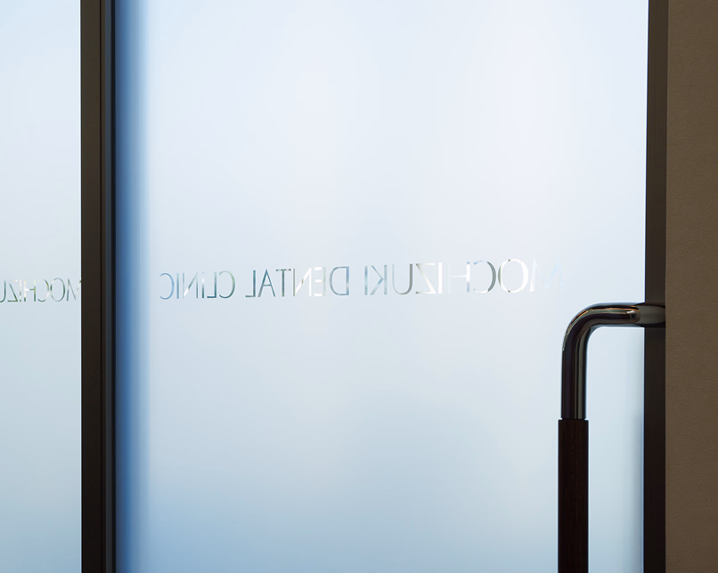 MOCHIZUKI DENTAL CLINIC のロゴが入った曇りガラスのエントランス扉